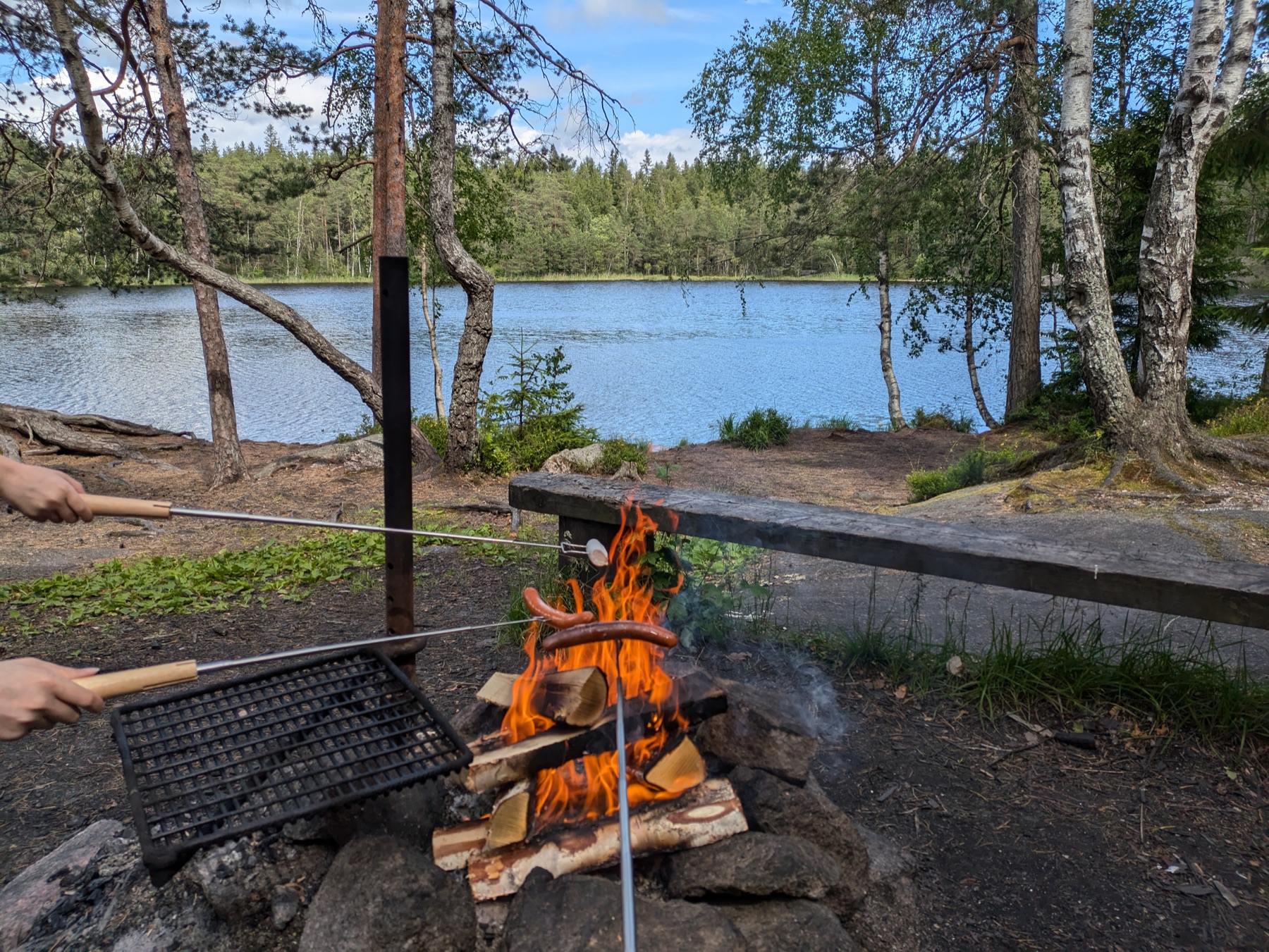 Grilling sausages over an open campfire beside a lake